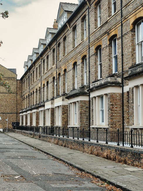 Exterior view of a row of historic brick residential buildings with multiple stories, featuring large sash windows, some with white trim, and decorative stone details. The buildings have slate roofs w